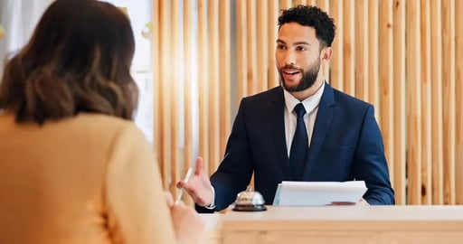 Web_Desktop-Woman at desk with man, paperwork and friendly reception service for hospitality. Check in, registration and receptionist with client
